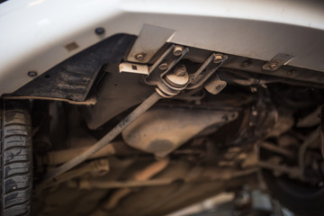 Car repair in the service station. Hands of a mechanic in overalls repairing the car on the lift without wheel, holding the tire and mechanical works.