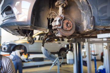 Car repair in the service station. Hands of a mechanic in overalls repairing the car on the lift without wheel, holding the tire and mechanical works.