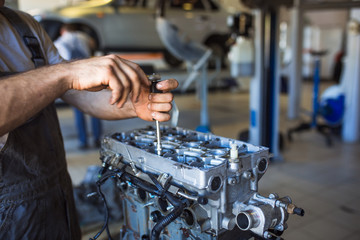 Mechanic with a tool in his hands repairing the motor of the machine. The process of working in the service station