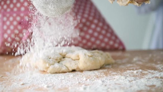 Girl with pink apron sprinkling flour on dogh, slow motion.