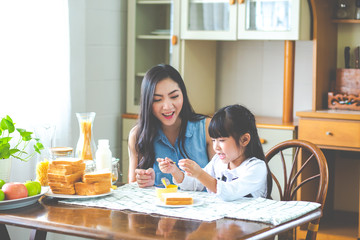 Mother and child daughter Spread butter on bread in the morning. happy family in the kitchen