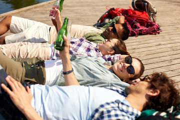 leisure, picnic and people concept - friends drinking beer and cider on lake pier in summer park