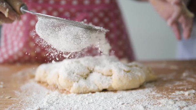 Girl with pink apron sprinkling flour on dogh, slow motion.