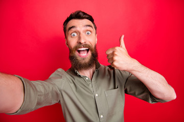 Photo of handsome overjoyed ecstatic man wearing grey shirt self shooting when thumbing up to you...