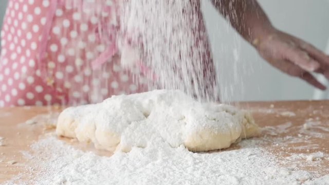 Girl with pink apron sprinkling flour on dogh, slow motion.