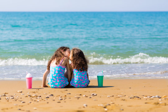little girls sit back on the sand and kiss, together with cocktails. Family vacation concept. happy sisters