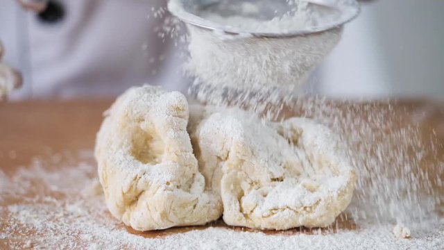 Girl in chef uniform sprinkling flour on dogh, slow motion.