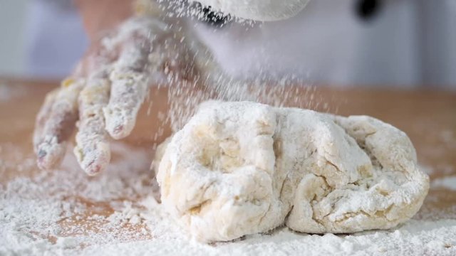 Girl in chef uniform sprinkling flour on dogh, slow motion.