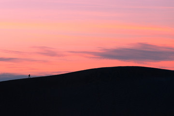 Fototapeta na wymiar One sunset hiker walking sand dune crest