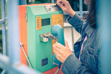 Woman using old and weathered oldstyle plublic pay phone in phone booth.