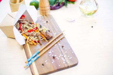 Naklejka na ściany i meble Wok. Noodles with vegetables and beef in take-out box on wooden table