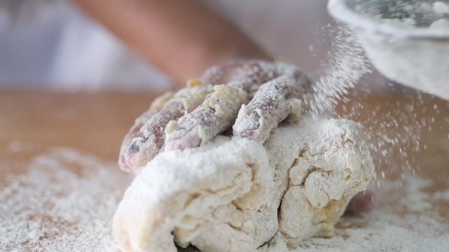 Girl in chef uniform sprinkling flour on dogh, slow motion.