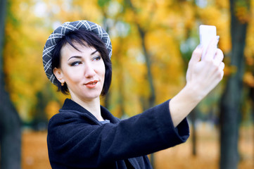 Beautiful woman taking selfie by smartphone and having fun in autumn city park, fall season, yellow leaves