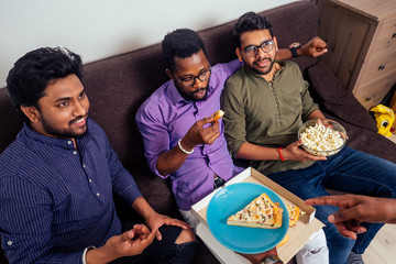 four african american males eating pizza at home party,throwing popcorn into each other