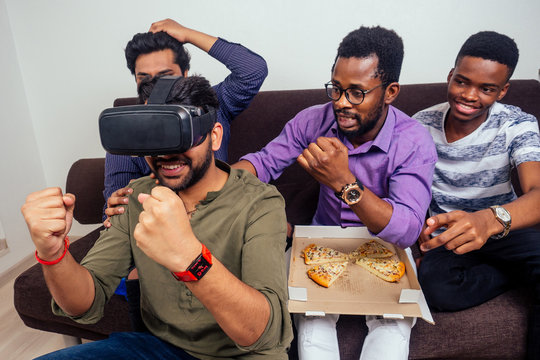four african american friends playing with vr helmet and eating pizza
