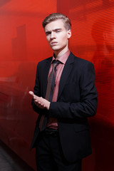 Young blond man standing and posing to the camera in the black suit on the red background