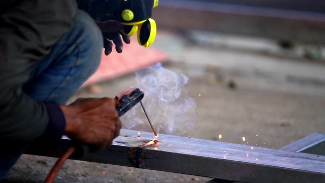 HD Slow motion close up shot of construction worker welder wearing welding mask using electric arc welding torch machine weld iron steel bar and making sparks fire flakes. Safety work concept.