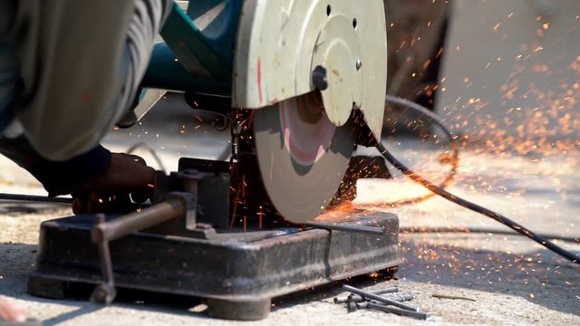 HD Slow motion close up shot of construction worker welder hands using electric angular grinding machine for cutting iron steel bar and making sparks fire flakes from welding. Safety work concept.