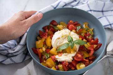 Frau isst Mozzarella Kugel mit roten und gelben Tomaten, Basilikum und Olivenöl auf Teller und  Marmor Hintergrund