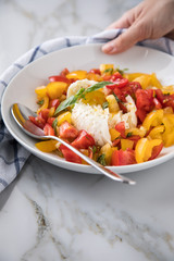 Frau isst Mozzarella Kugel mit roten und gelben Tomaten, Basilikum und Olivenöl auf Teller und  Marmor Hintergrund