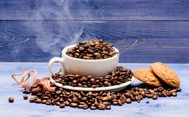 Cafe drinks menu. Fresh roasted coffee beans. Cup full coffee brown roasted beans white clouds of smoke blue wooden background. Coffee for inspiration and energy charge. Degree of roasting grain
