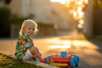 Beautiful toddler child, playing with plastic toys, blocks, cars on sunset