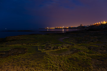The nocturnal lights of La Mata near the Spanish city of Torrevieja. The lights of the coast are reflected in the smooth water. Some stars are sparkling in the sky.