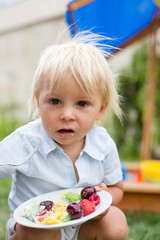 Little boy celebrating his birthday in home's garden with big cake
