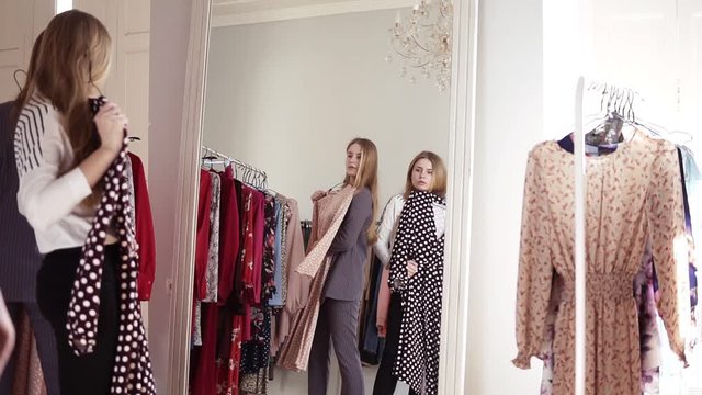 Sisters or friends are trying the fashionable dresses while looking in mirror in clothes boutique or mall. Decising to buy or not. Mirror reflection footage