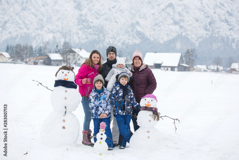 Poster Family with children, building snowman in the park in little village in Austria