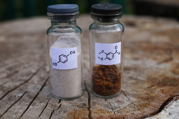 Two glass jars with crystalline substances: white hydroquinone, brown aromatic aldehyde.