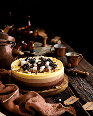 Beautiful still life with homemade delicious three chocolates cheese cake on wooden stand on rustic table