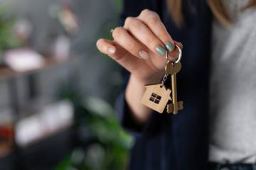 Concept of renting an apartment. House key in womans hands. Young woman. Modern light lobby interior. Real estate, hypothec, moving home or renting property.