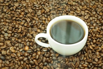 Cup of hot coffee on coffee beans with smoke from the roasting heat.