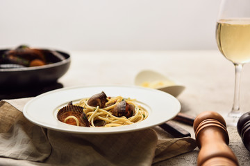 selective focus of delicious pasta with seafood served with white wine on napkin isolated on grey