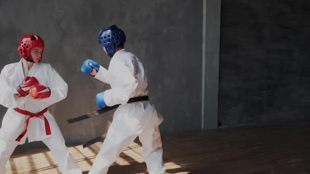 Slow motion. Aggressive angry box fighters hitting in sparring. Asian boy makes strong extreme kick into rival face. Hard powerful duel. Martial mix arts. Helmet, feets, gloves, kimono.