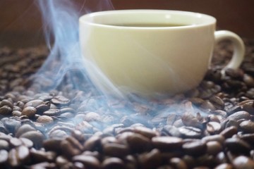 Cup of hot coffee on coffee beans with smoke from the roasting heat.