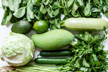 Fresh green vegetables variety on rustic white background from overhead, celery, avocado, cabbage, mango, cucumber, spinach, lime, squash. Healthy, vegetarian concept. Flat lay, top view