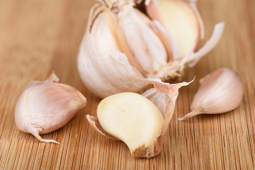 A head of garlic, several cloves of unpeeled garlic and a clove peeled on a wooden background.