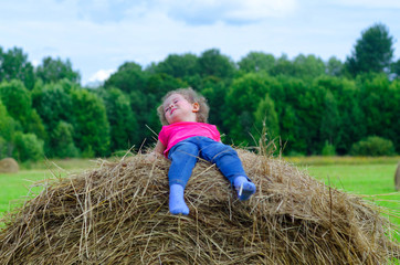 Naklejka na ściany i meble little girl lies on a haystack under a blue sky on a sunny summer day. Baby play at hay bales in harvest time in Germany during Oktoberfest. soft focus.