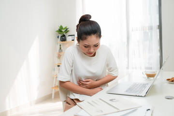 Asian woman with stomach ache or feeling hurting stomach in office table