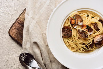 top view of delicious pasta with mollusks on napkin on wooden cutting board on white background