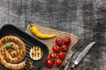 Snail sausage garnish with red peppercorn and basil leaf in pan on textured backdrop