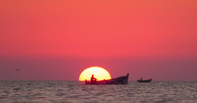 Fisher boat passing in front of the sun during an amazing sunset in Africa, big sun, orange light