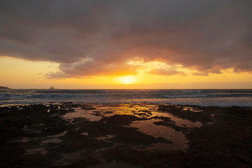 Vibrant, golden sunrise over the limestone coasts of El Medano, Tenerife, Canary Islands, Spain. Mellow light sunrise over the Atlantic with calm waters and a silhouetted oil rig in the distance.