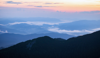 Fototapeta premium mountain valley covered with fog in the orange and blue twilight light. mountain silhouette