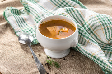 Fresh fish soup with spices in white bowl and spoon on grey tablecloth