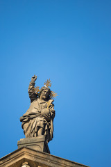 Fototapeta na wymiar Statue on roof of St. Francis of Assisi church in Prague with blue sky in background