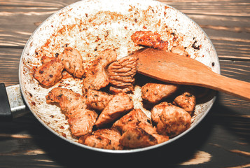 Fried chicken breast in oil and spices. Unhealthy food. Burnt pan. Damaged kitchenware. Wooden background.