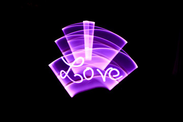 Word love written with a led lamp during a lightpainting session at night. Abstract curved shape drawn with a light saber.